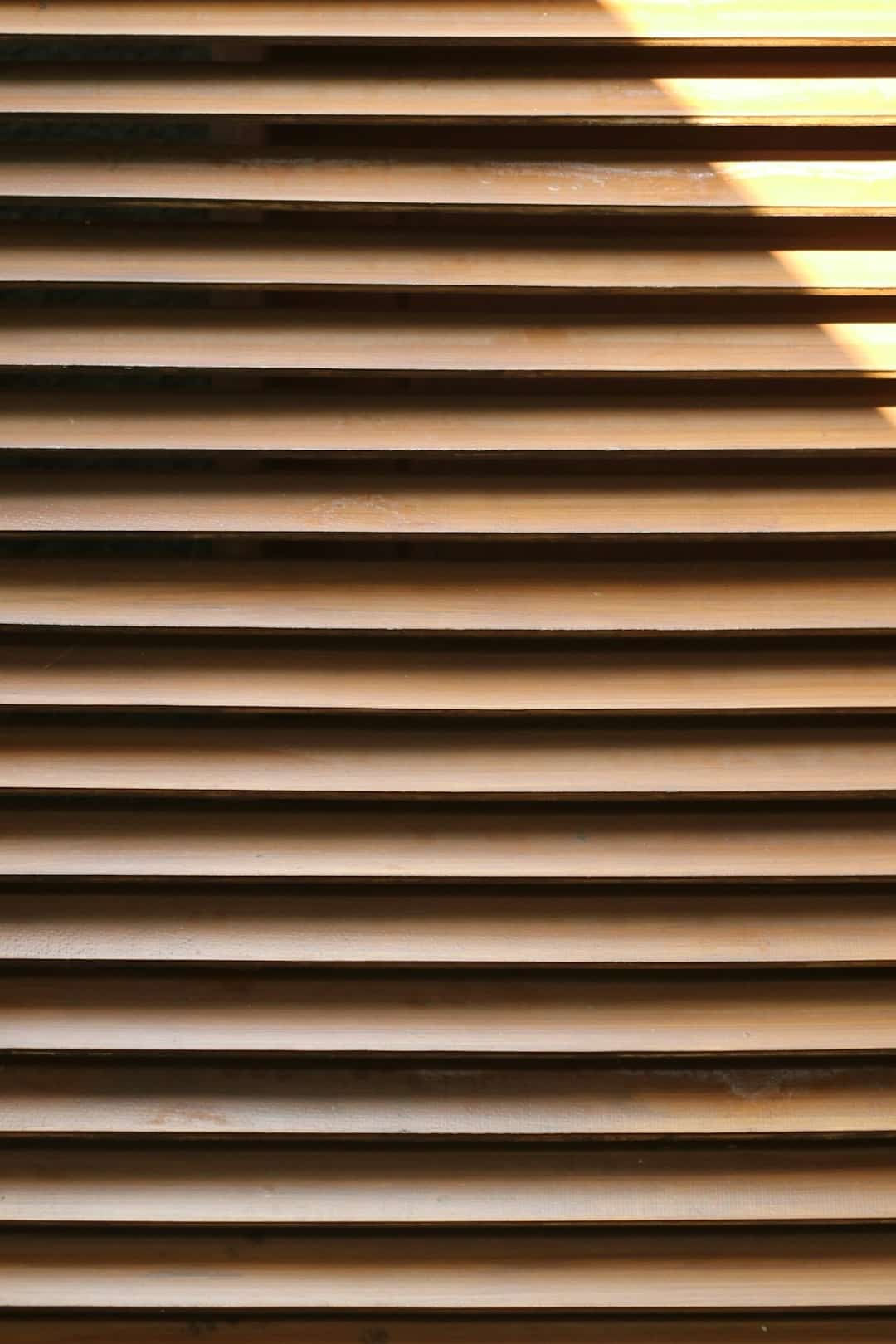 Light brown wooden louvered shutters with visible dust particles.