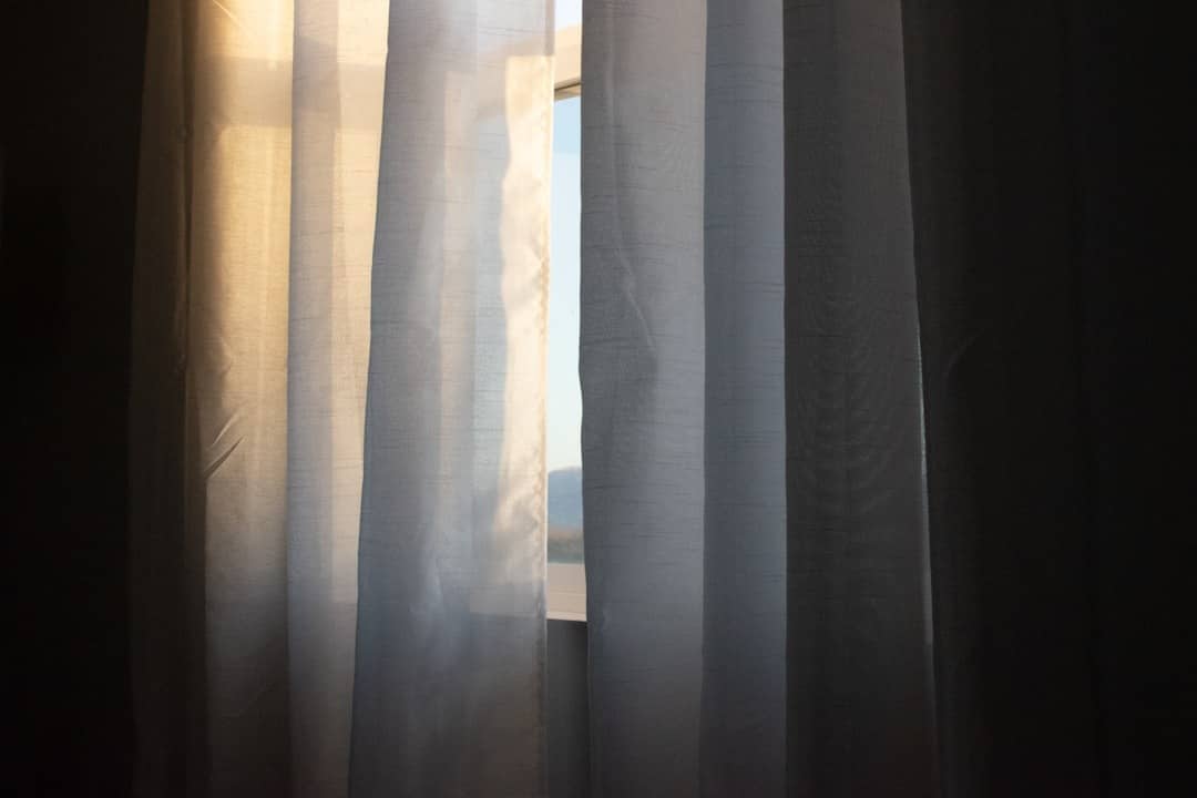 Sunlight filters through sheer curtains showing a distant landscape.